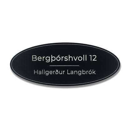 Lítið sporöskjulaga hurðaskilti svart með hvítu heimilisfangi.